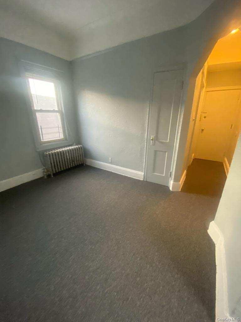 Unfurnished bedroom featuring baseboards, dark carpet, and radiator