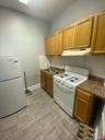 Kitchen featuring dark countertops, tasteful backsplash, a sink, under cabinet range hood, and white appliances