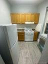 Kitchen with white appliances, brown cabinetry, baseboards, light wood-type flooring, and under cabinet range hood