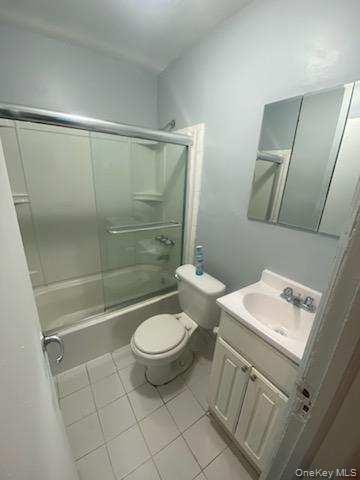 Bathroom with tile patterned flooring, bath / shower combo with glass door, toilet, and vanity