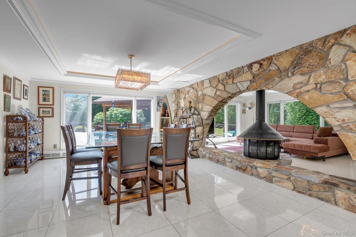 Dining Room with a raised ceiling, a wood burning fireplace, ornamental molding, light tile patterned floors, and a chandelier