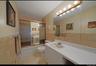 Bathroom with tile walls, bath / shower combo with glass door, vanity, light tile patterned flooring, and a wainscoted wall