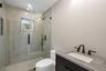 Bathroom featuring vanity, a marble finish shower, and tile walls