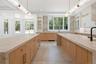 Kitchen with light stone countertops, glass insert cabinets, a spacious island, decorative light fixtures, and light brown cabinetry