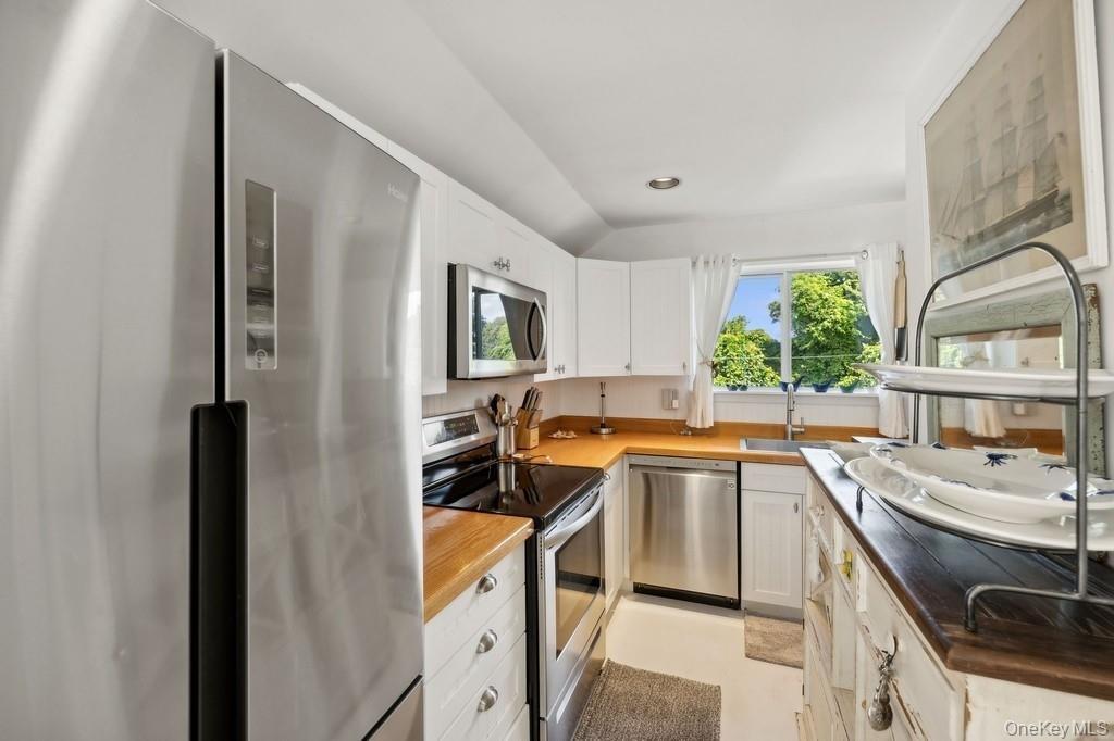 Kitchen featuring appliances with stainless steel finishes, white cabinetry, lofted ceiling, recessed lighting, and wooden counters
