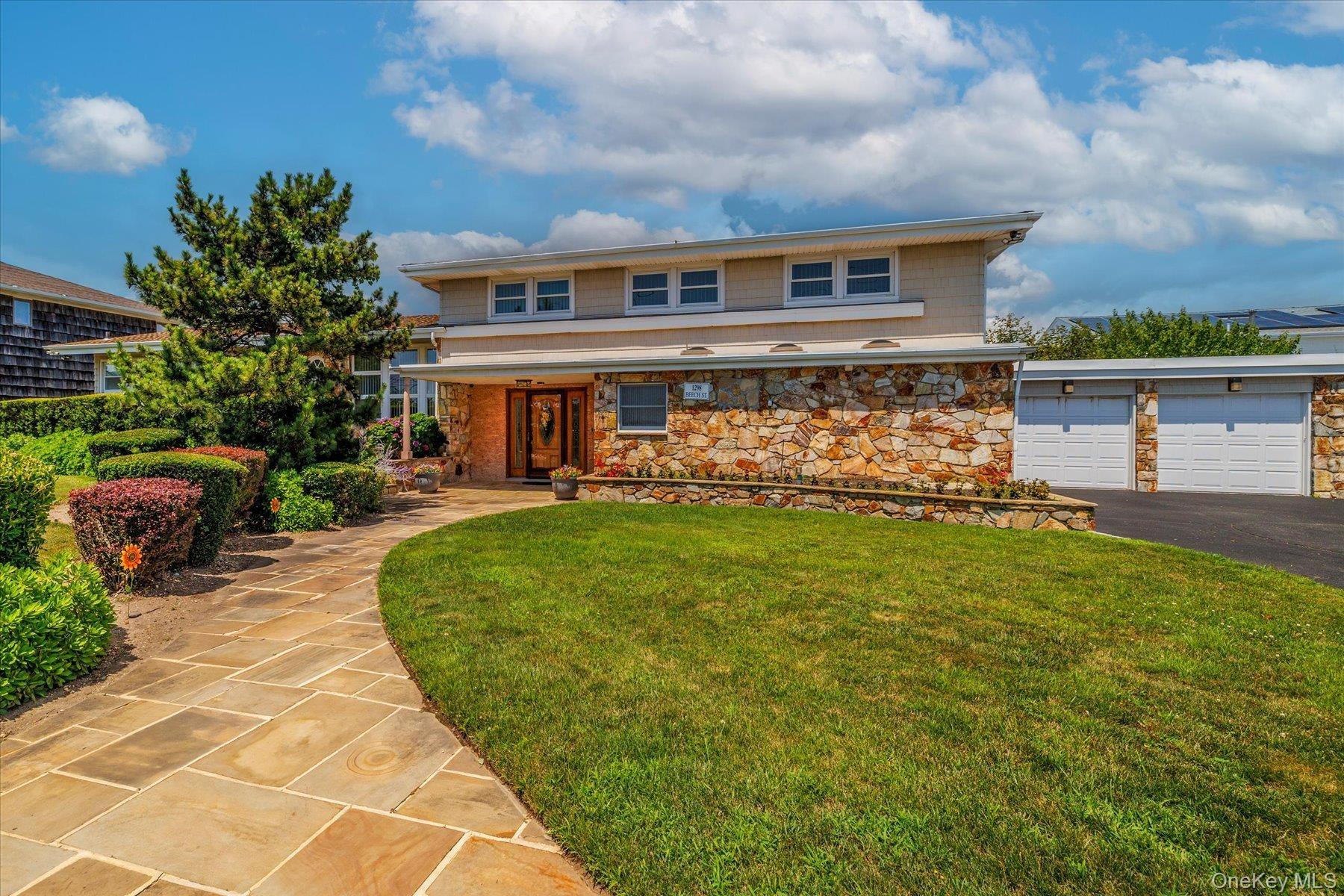 View of front of property featuring a front lawn, stone siding, a garage, and asphalt driveway