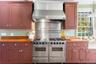 Kitchen with range with two ovens, wall chimney exhaust hood, wooden counters, and decorative light fixtures