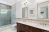 Bathroom with a shower stall, tile walls, double vanity, light tile patterned floors, and a chandelier