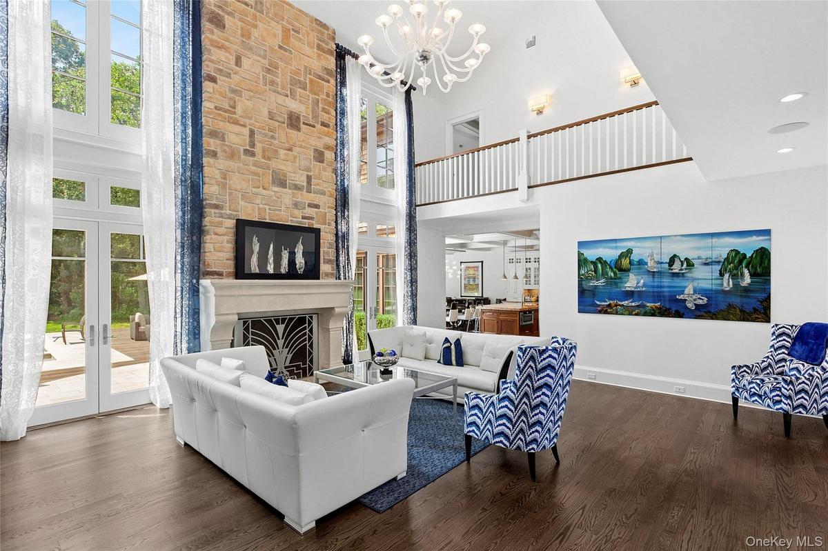 Living room with plenty of natural light, dark wood finished floors, a large fireplace, a chandelier, and a towering ceiling