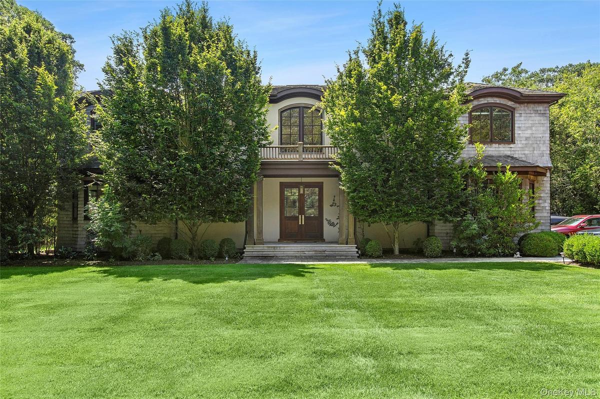 View of front of property with a front lawn, a balcony, french doors, stucco siding, and a porch