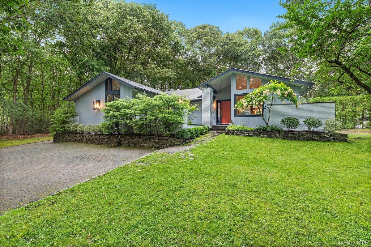 Mid-century home with a front yard, decorative driveway, and view of scattered trees