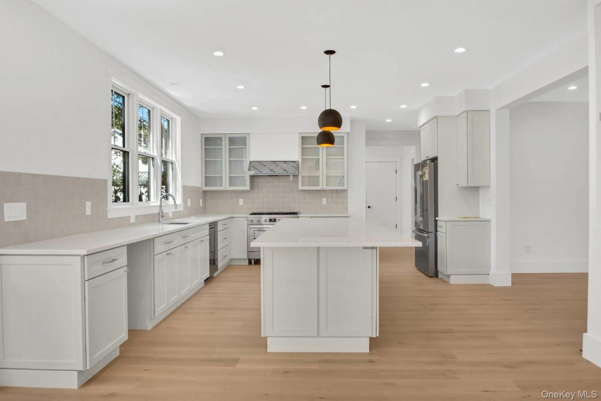 Kitchen featuring a kitchen island, glass insert cabinets, white cabinets, light wood-style flooring, and decorative backsplash