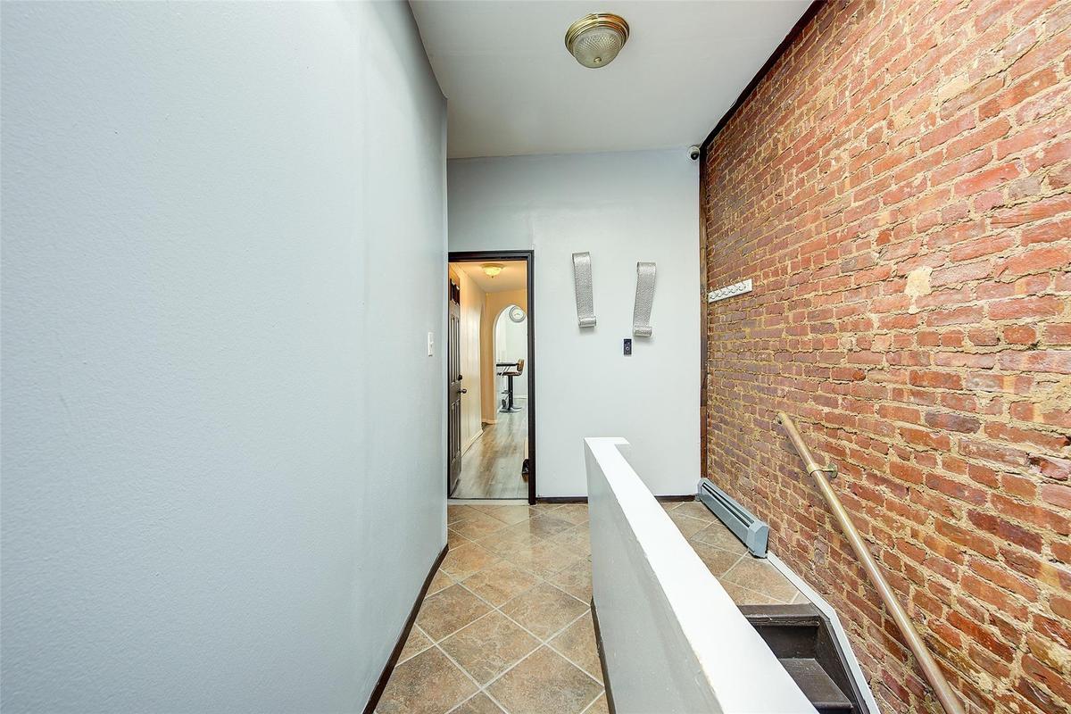Hallway featuring baseboard heating, an upstairs landing, arched walkways, and brick wall