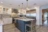 Kitchen with white cabinetry, hanging light fixtures, built in appliances, and wall chimney exhaust hood