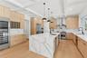 Kitchen featuring light stone counters, hanging light fixtures, modern cabinets, light brown cabinetry, and beamed ceiling