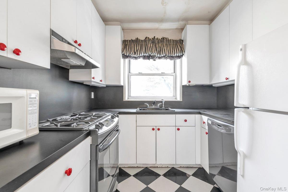Kitchen featuring white appliances, dark countertops, light flooring, and under cabinet range hood