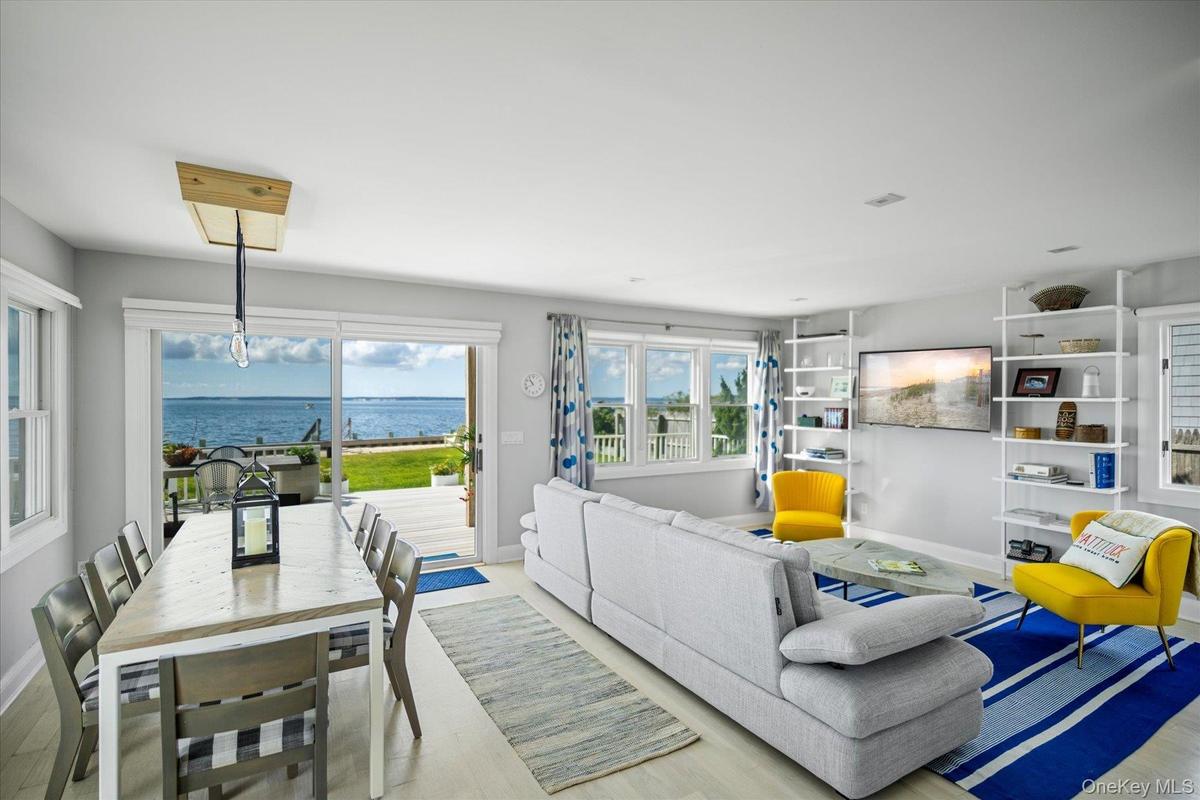 Sun filled living room with large windows and sliders framing sweeping bay views. Furnishings included in sale.