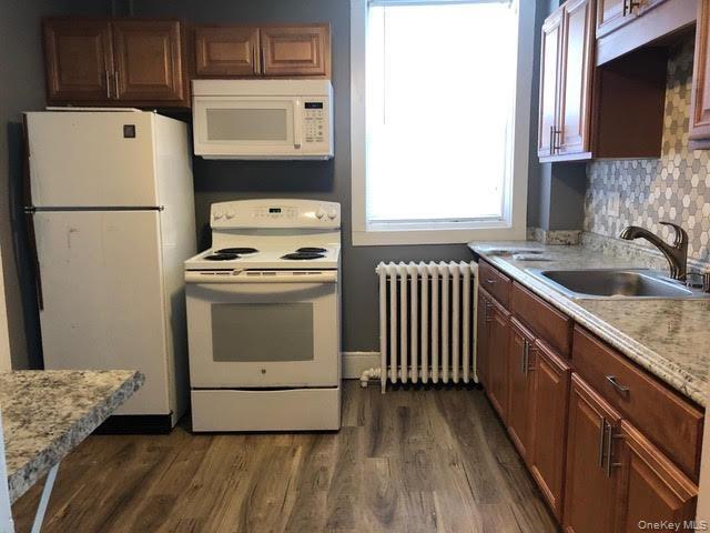 First Floor Front Building Kitchen featuring white appliances, light countertops, radiator, dark wood-style floors, and tasteful backsplash