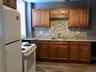 First Floor Front Building Kitchen featuring decorative backsplash, white appliances, dark wood-type flooring, and brown cabinets