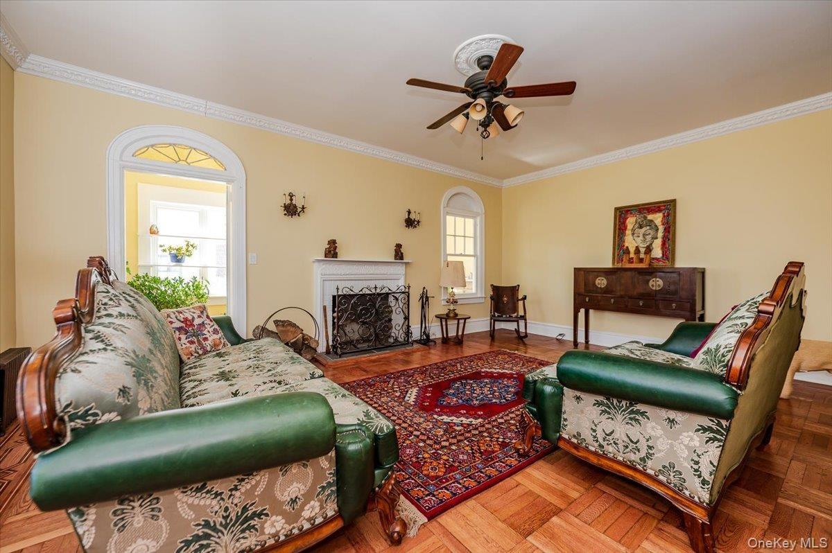 Formal Living area featuring a fireplace, custom redone floors with marquetry inlay, ceiling fan, and beautiful crown molding