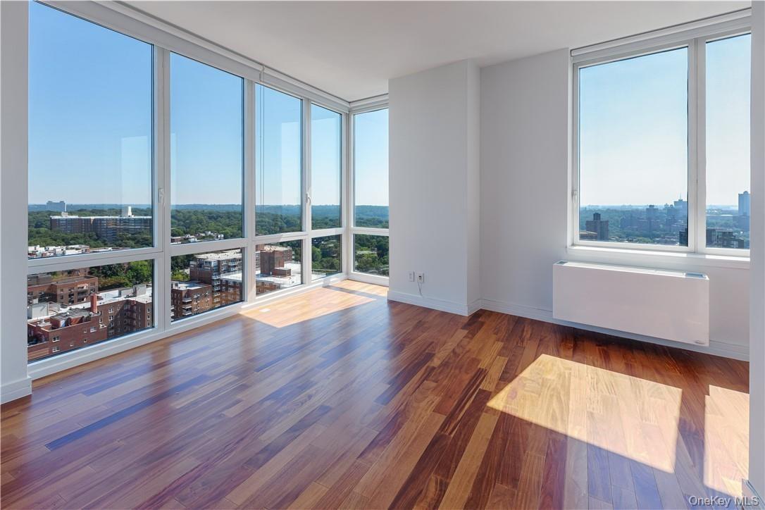 Empty room with plenty of natural light, a wall of windows, dark hardwood / wood-style flooring, and radiator heating unit