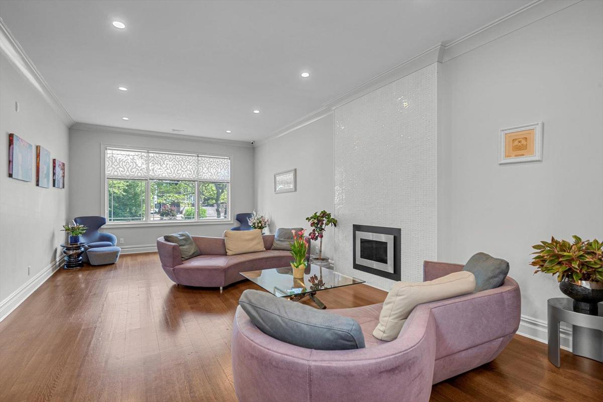 Living room with crown molding, wood finished floors, a large fireplace, and recessed lighting