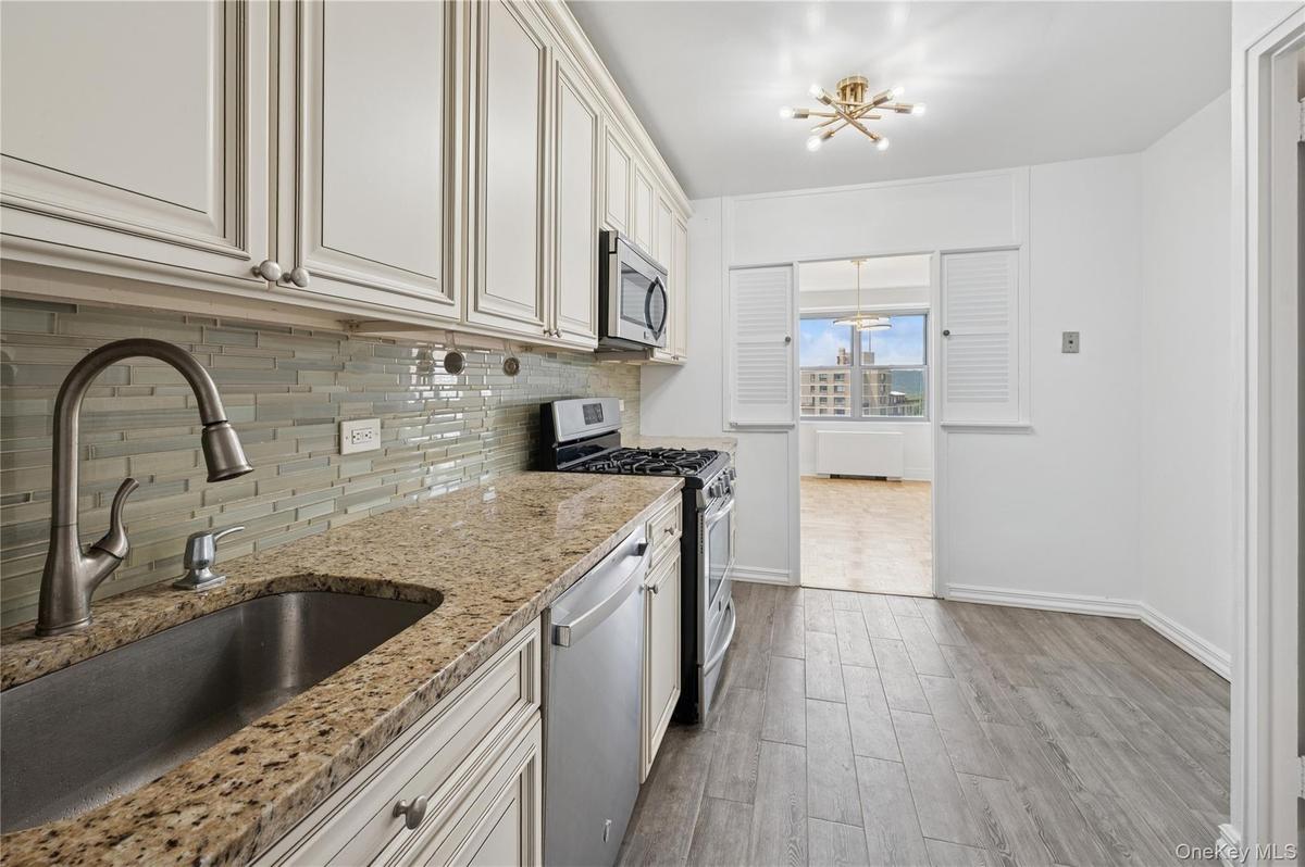 Kitchen featuring stainless steel appliances, a chandelier, backsplash, light wood-type flooring, and light stone countertops