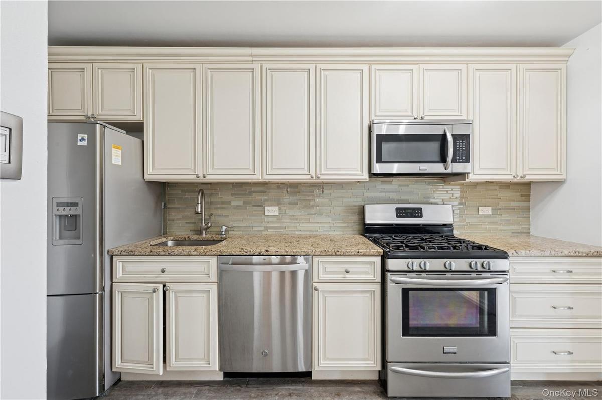 Kitchen with appliances with stainless steel finishes, light stone counters, tasteful backsplash, and cream cabinets