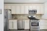 Kitchen with appliances with stainless steel finishes, light stone counters, tasteful backsplash, and cream cabinets