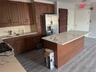 Kitchen featuring stainless steel fridge, dark wood finished floors, a center island, black range with gas cooktop, and light stone countertops