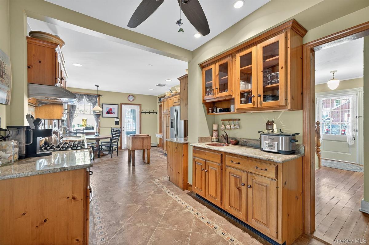 Kitchen featuring decorative light fixtures, glass insert cabinets, inlaid floor details, brown cabinetry, and light tile patterned floors