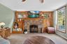 Carpeted living room featuring a brick fireplace, wooden walls, a baseboard radiator, and ceiling fan