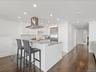 Kitchen featuring tasteful backsplash, appliances with stainless steel finishes, a peninsula, island range hood, and white cabinets