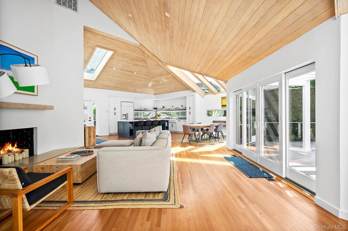 Living room with vaulted ceiling, a warm lit fireplace, plenty of natural light, and wood flooring