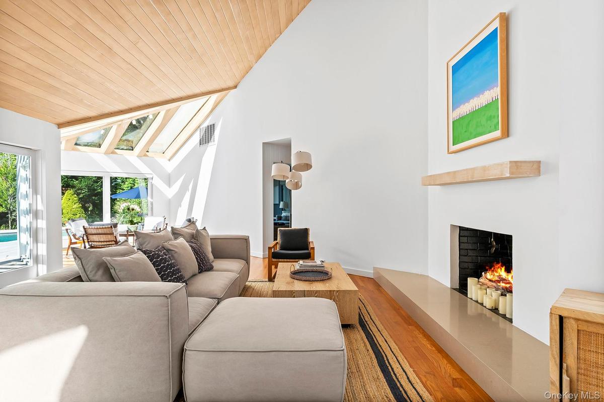 Living room with a lit fireplace, wood finished floors, wood ceiling, a skylight, and high vaulted ceiling