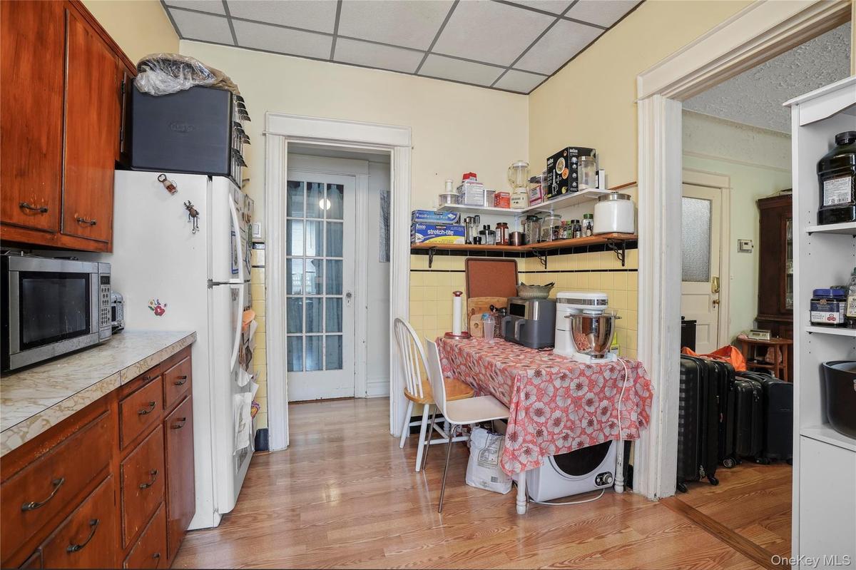 Kitchen featuring stainless steel microwave, freestanding refrigerator, a paneled ceiling, light wood-style floors, and tile countertops