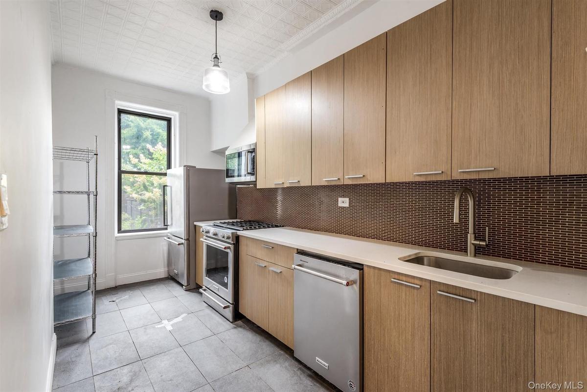 Kitchen featuring appliances with stainless steel finishes, backsplash, modern cabinets, light tile patterned floors, and hanging light fixtures