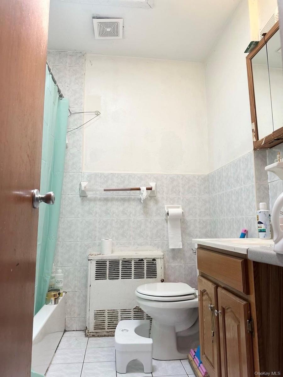 Bathroom with light tile patterned floors, tile walls, shower / bath combination with curtain, vanity, and radiator heating unit