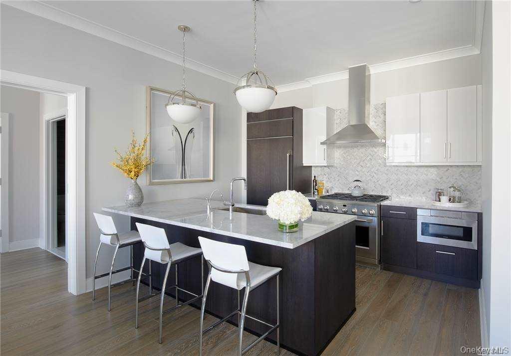 Kitchen featuring backsplash, a breakfast bar area, wall chimney range hood, dark brown cabinetry, and dark wood-type flooring