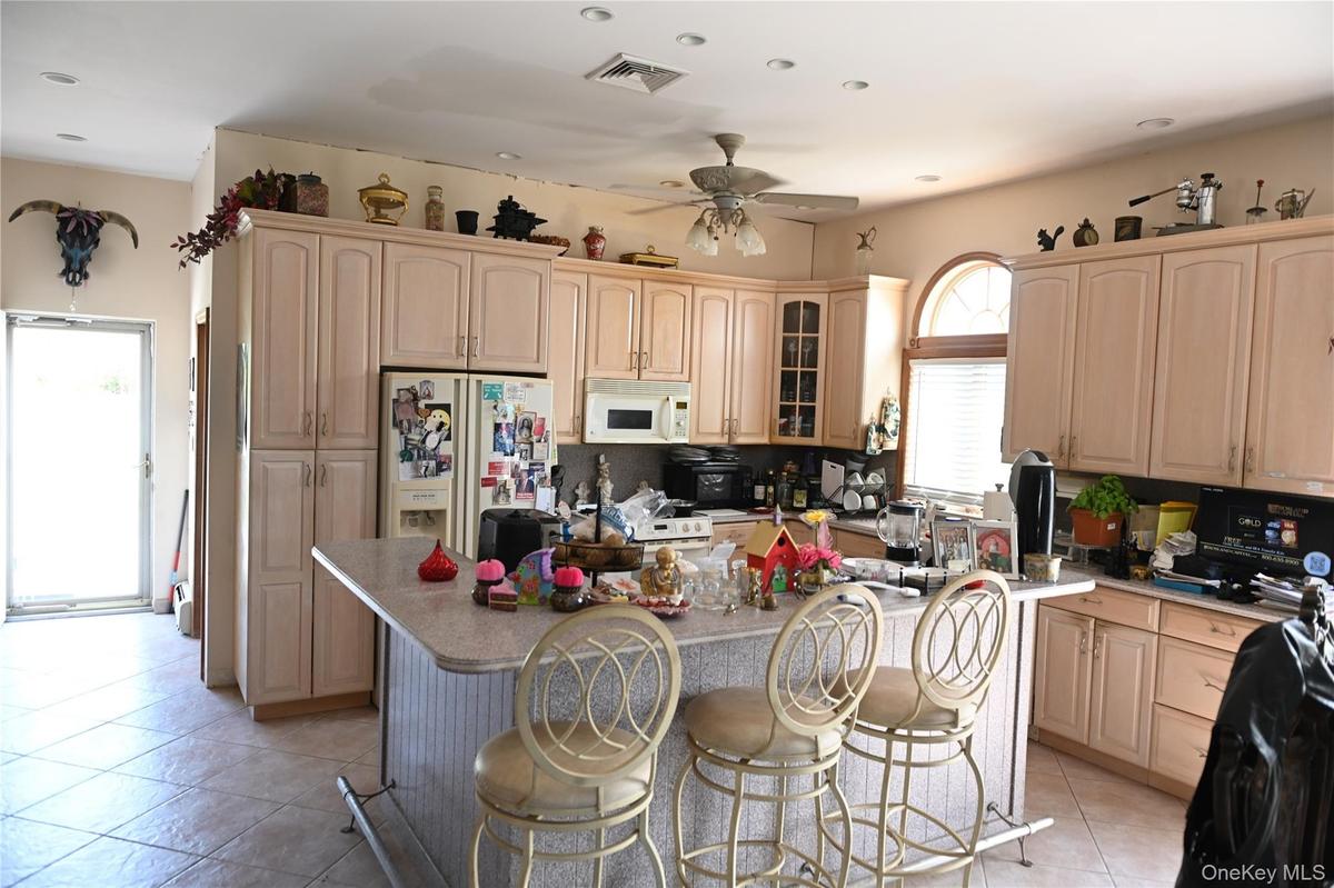 Kitchen with a breakfast bar, light brown cabinets, white appliances, glass insert cabinets, and light tile patterned floors