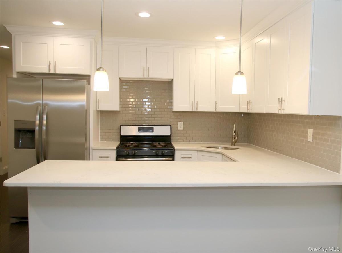 Kitchen featuring backsplash, white cabinets, appliances with stainless steel finishes, recessed lighting, and light stone counters