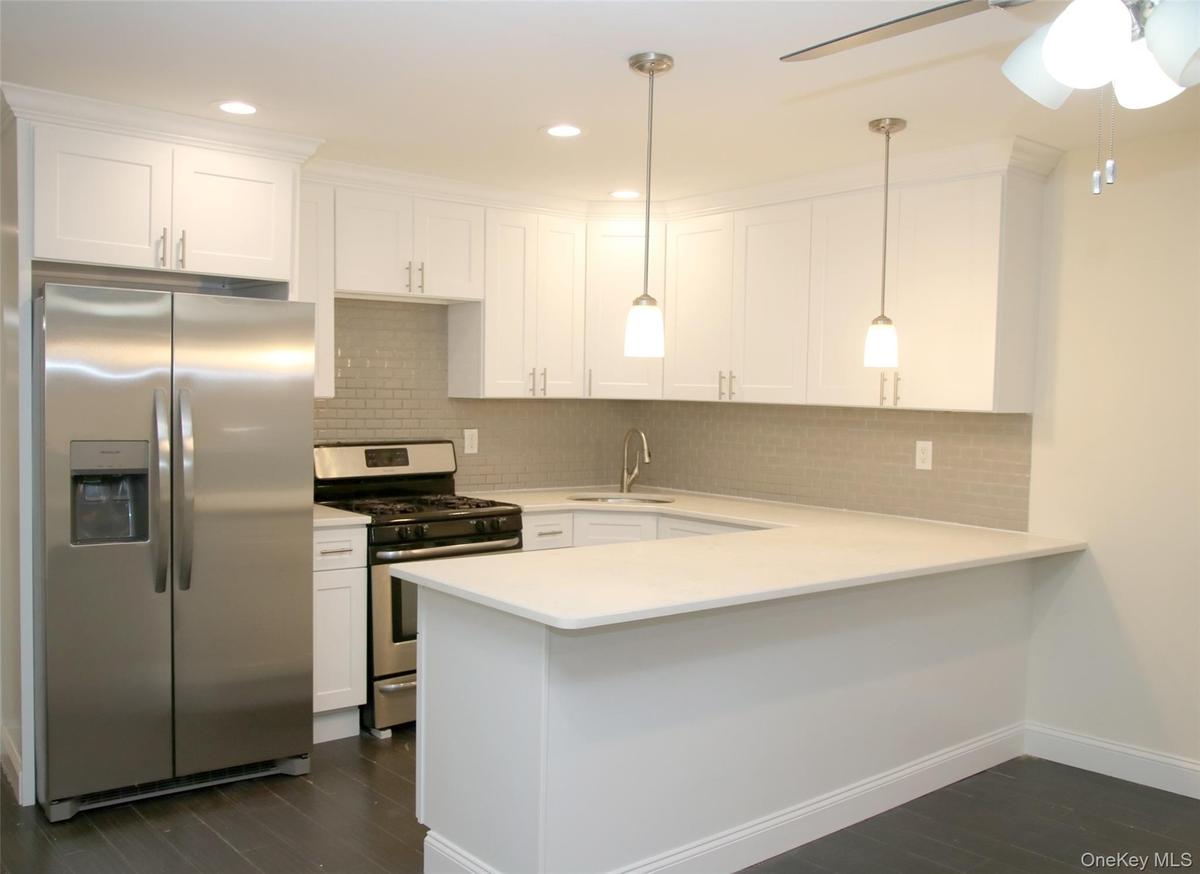 Kitchen featuring stainless steel appliances, backsplash, a peninsula, white cabinetry, and recessed lighting