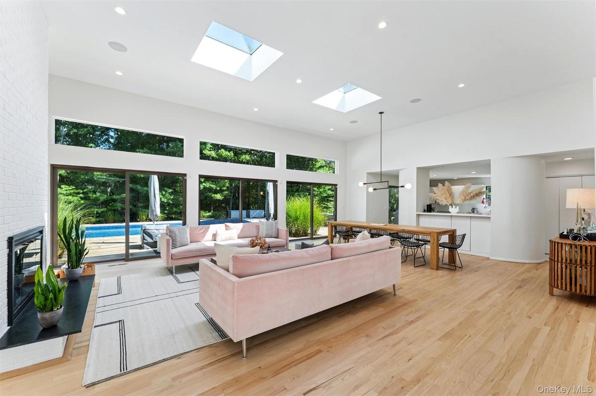 Living room featuring recessed lighting, a towering ceiling, light wood-style flooring, plenty of natural light, and a skylight