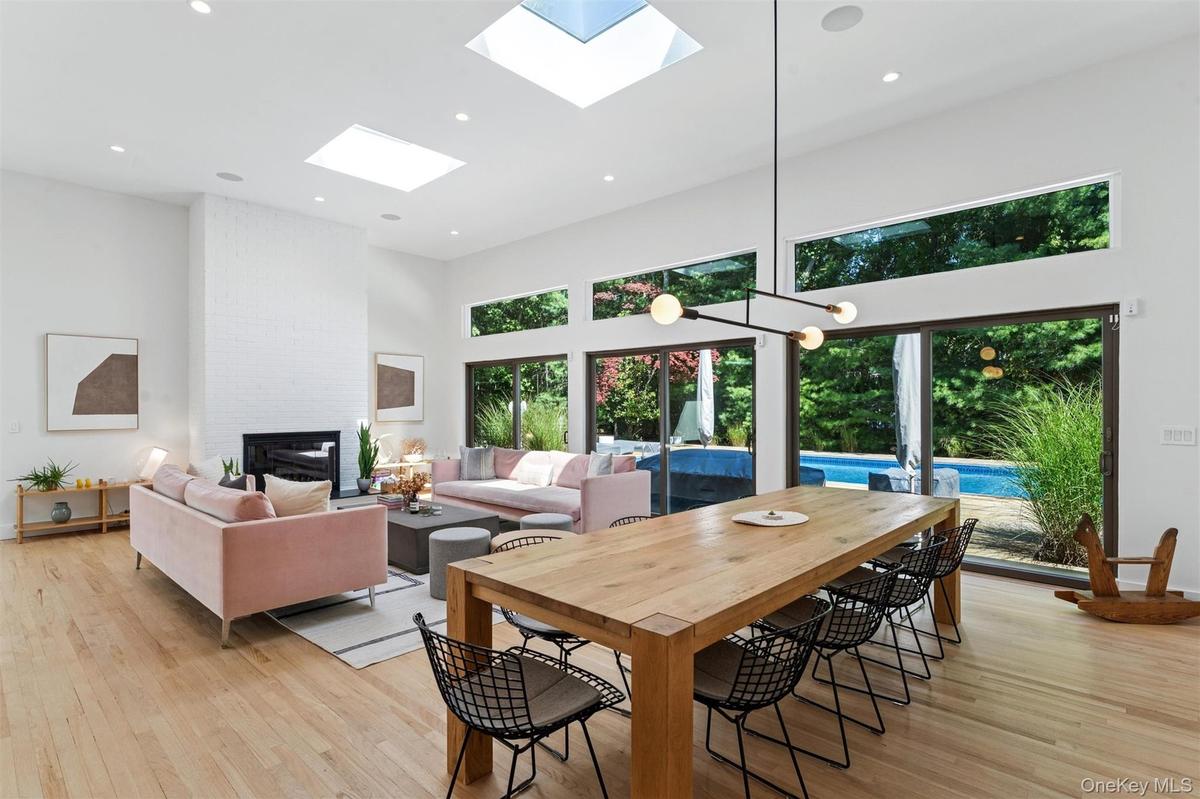 Dining room featuring a towering ceiling, a brick fireplace, light wood finished floors, recessed lighting, and a skylight