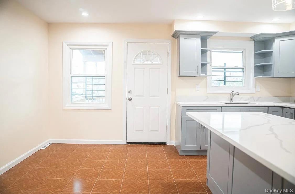 Kitchen featuring a sink, gray cabinets, open shelves, tile patterned floors, and baseboards