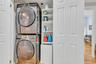 Laundry room with stacked washer and clothes dryer, wood finished floors, and crown molding