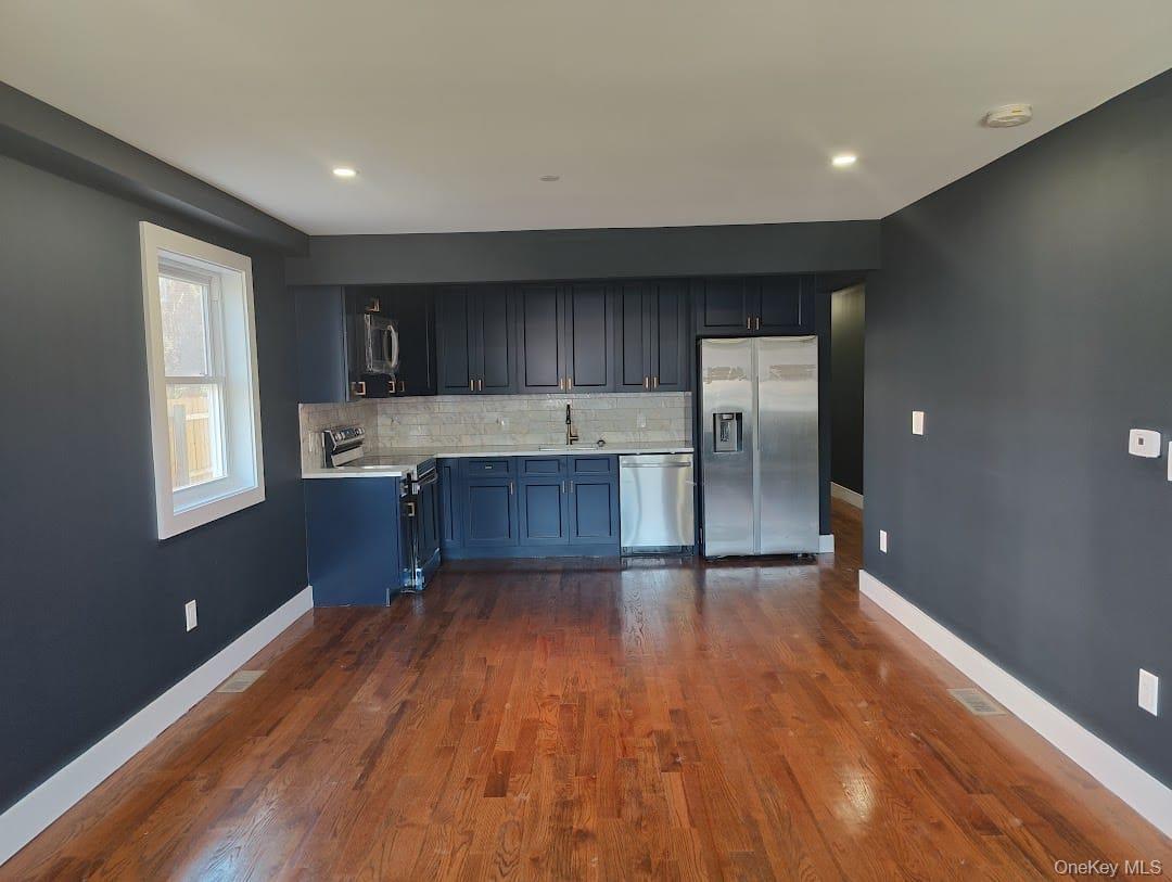 Kitchen with decorative backsplash, appliances with stainless steel finishes, dark wood finished floors, recessed lighting, and blue cabinetry