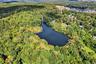 Aerial view of property and surrounding area featuring a nearby body of water and a heavily wooded area
