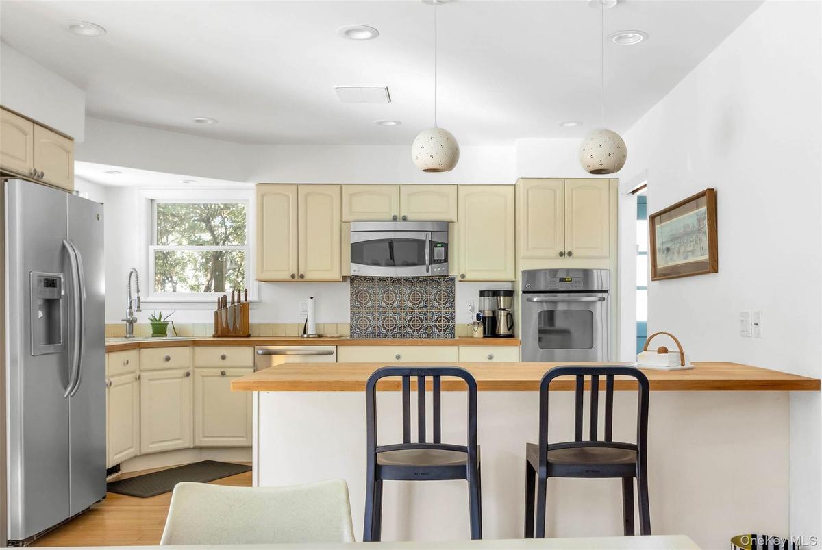 Kitchen with wood counters, decorative light fixtures, sink, stainless steel appliances, and cream cabinets