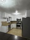 Kitchen with appliances with stainless steel finishes, tasteful backsplash, white cabinetry, wood tiled floors, and dark stone counters